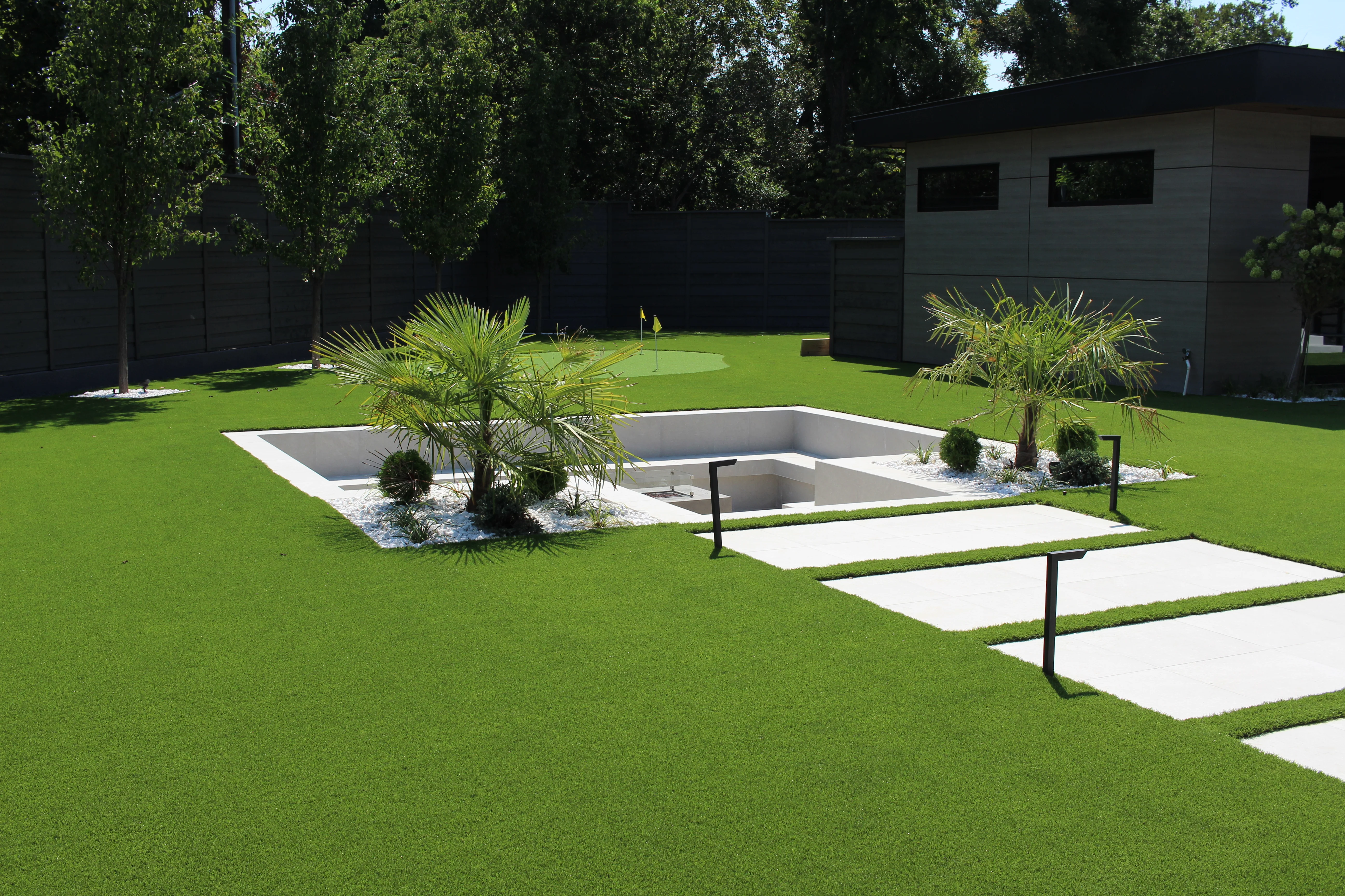Sunken pool with white concrete edges, tropical plants, and geometric stepping stones in modern backyard