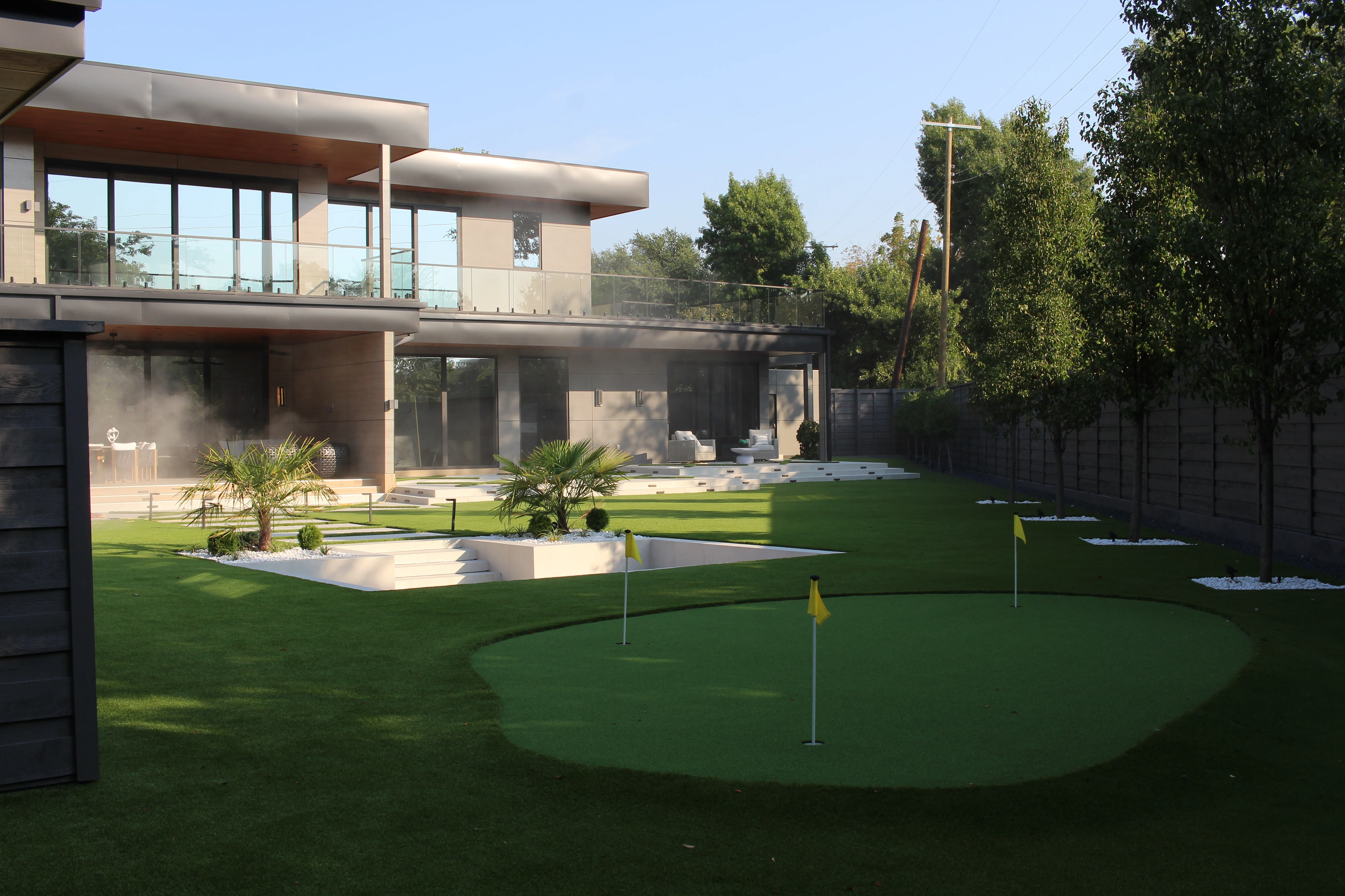 Modern backyard with synthetic putting green, tropical plants, and manicured lawn