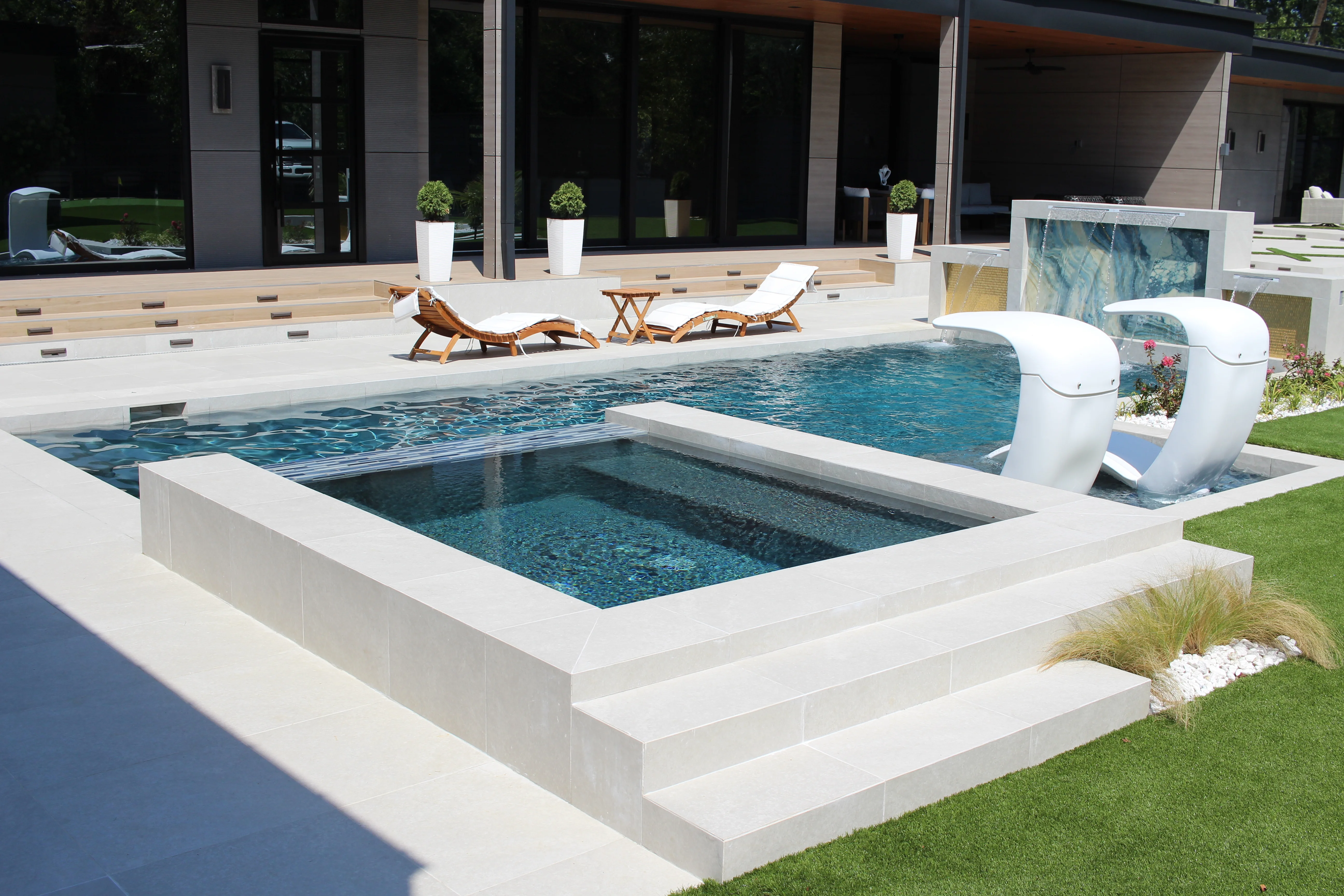Modern geometric swimming pool with white deck, integrated spa, and lounge seating area