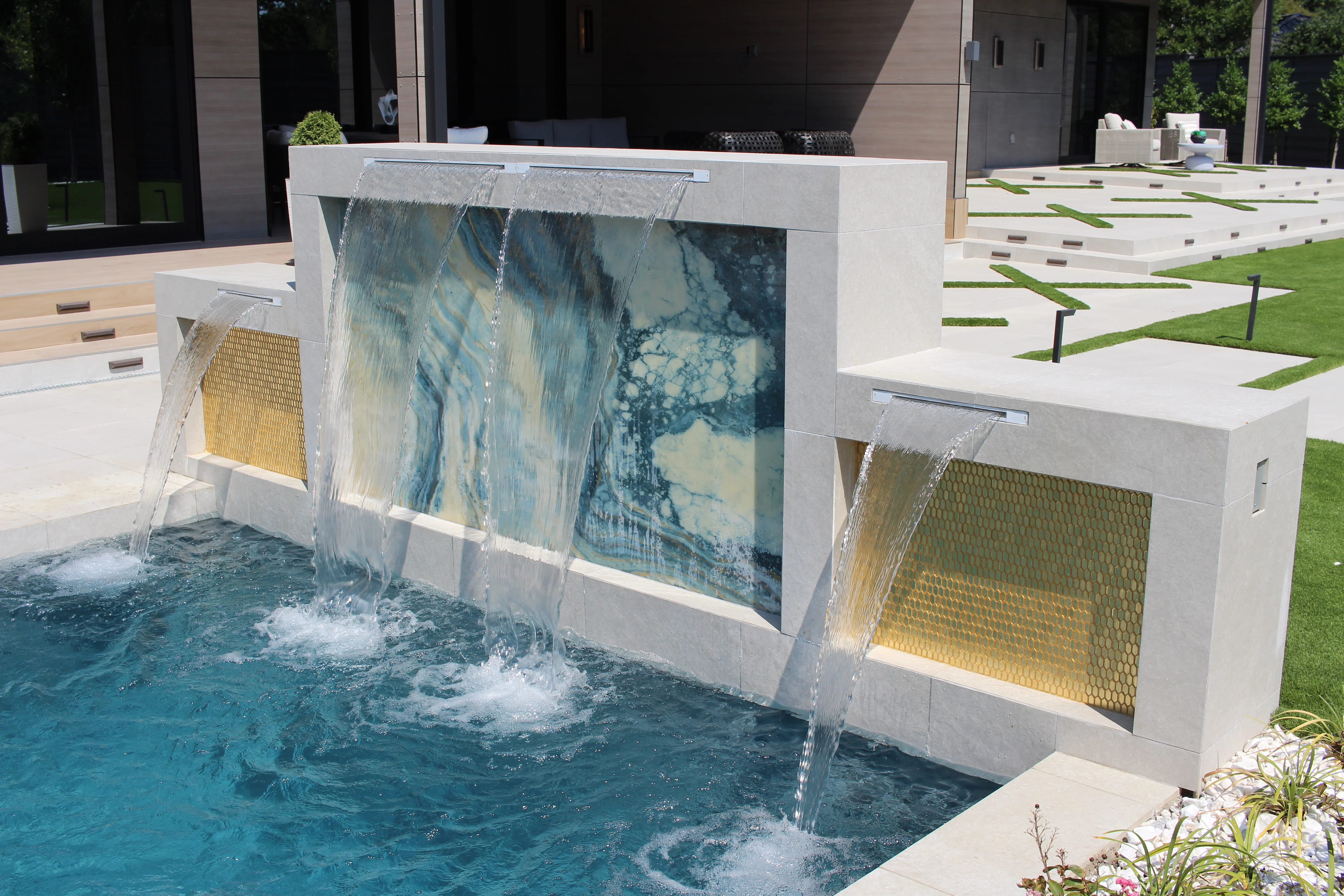 Luxury pool with dual waterfall features, illuminated glass panels, and manicured landscape